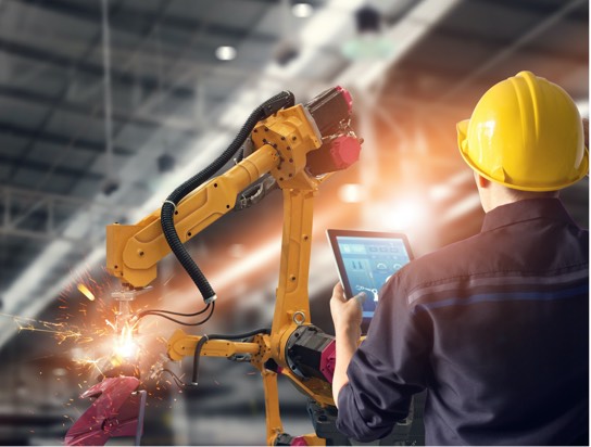 A view from behind of someone wearing a hardhat and holding a digital tablet standing in front of a piece of machinery